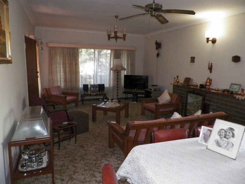 Spacious living room featuring a brick fireplace, ceiling fan, and wall sconces, offering a traditional layout with potential for modern updates.