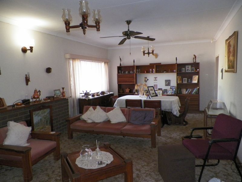 A spacious living room featuring a brick fireplace, built-in wooden shelving, and a ceiling fan, offering a traditional layout with potential for modernization.