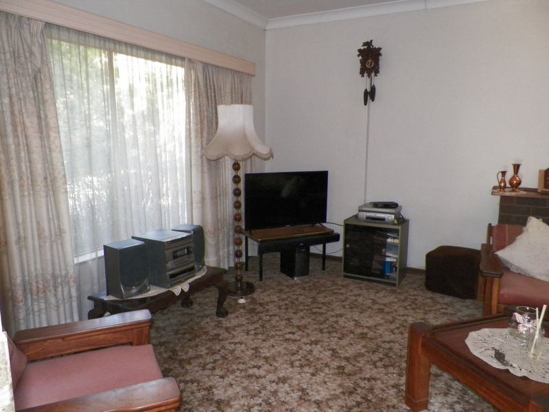 A living room featuring patterned carpet flooring and coving, offering a dated interior space ready for modernization.