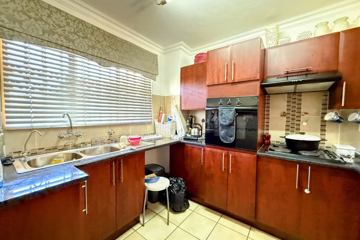 A functional kitchen featuring dark wood cabinetry, granite countertops, a built-in oven, hob, extractor fan, and a double sink with tiled backsplash.