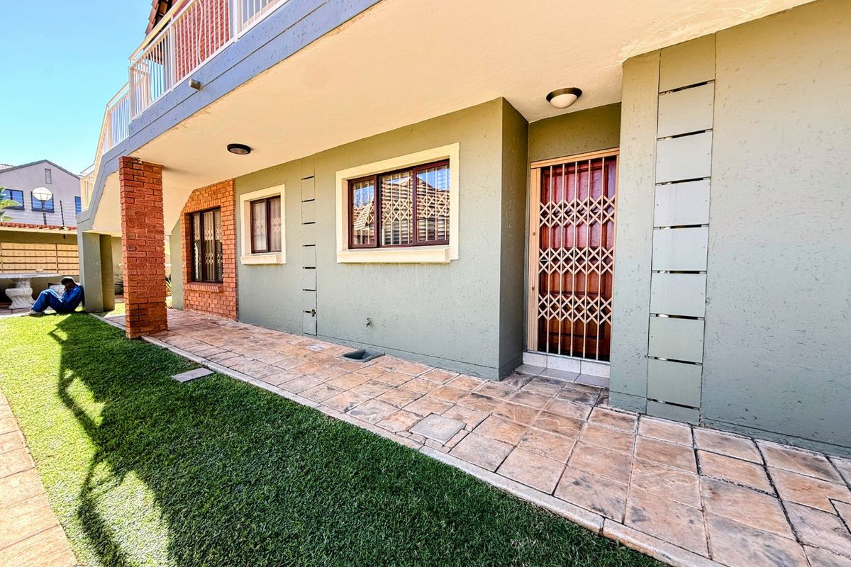 Rear exterior view of the apartment featuring a paved patio area, brick support pillar, and secure entrance gate leading to the lawn.