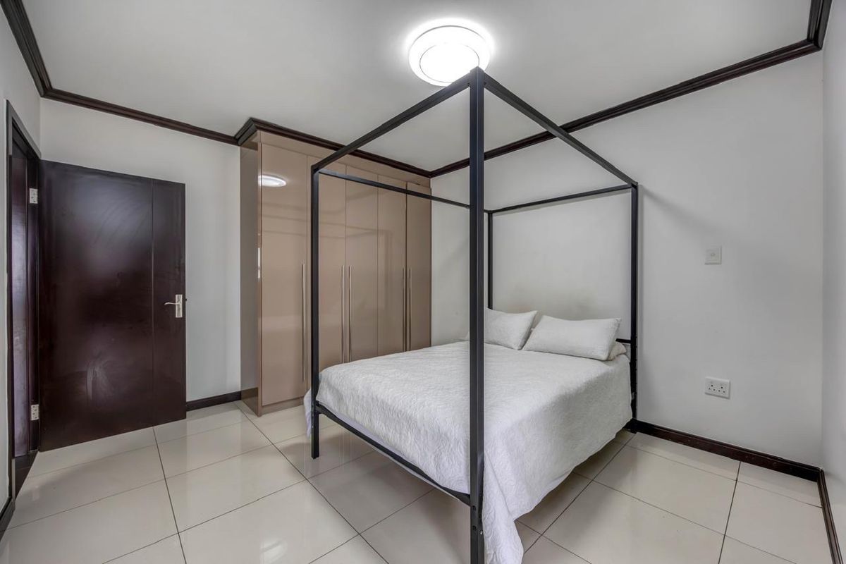 A well-maintained bedroom featuring neutral tiled flooring, dark wood door frames, and modern built-in cupboards with a glossy finish.