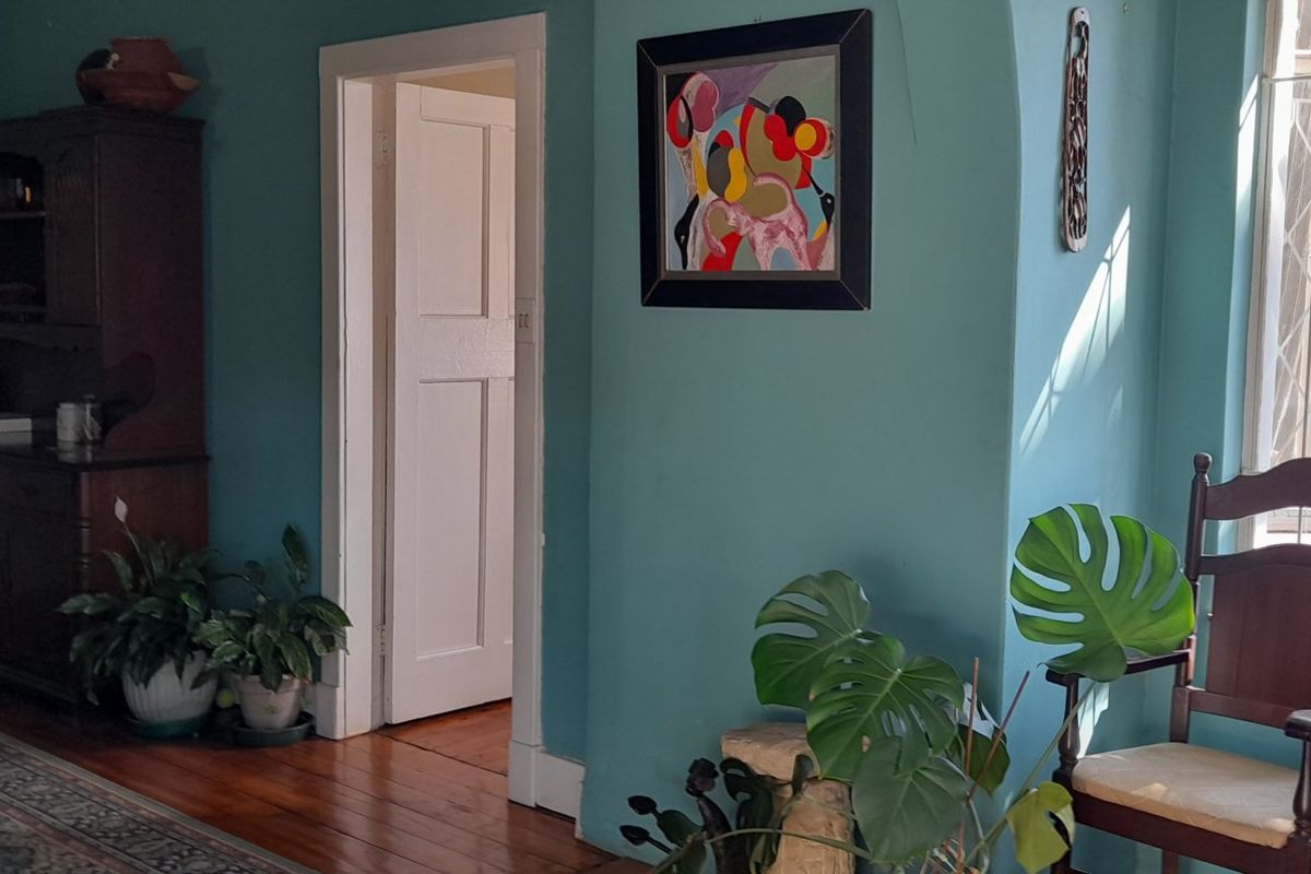 A living area featuring original hardwood flooring, an arched entryway, and a classic leaded glass window, finished with bold teal wall paint.