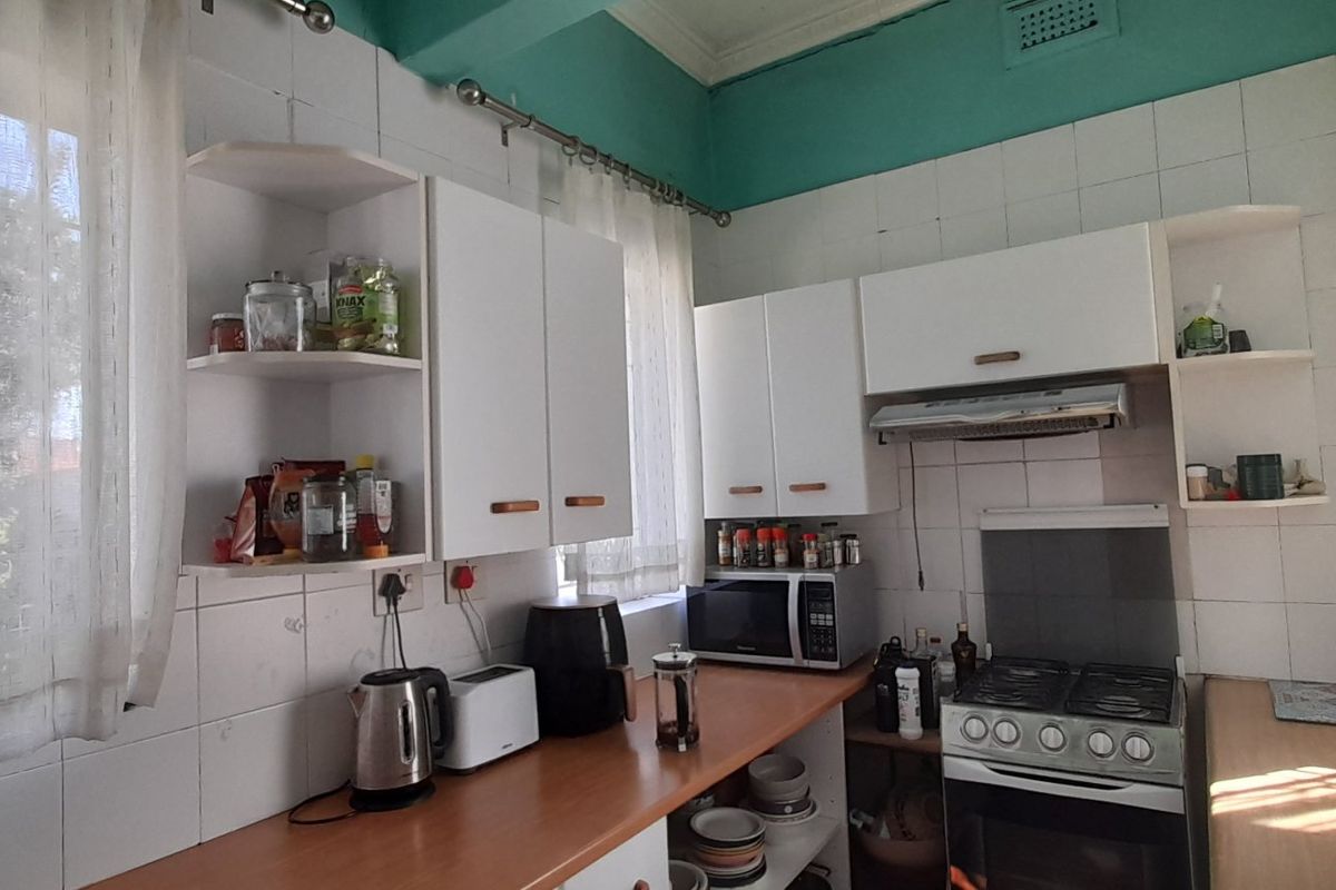 A functional kitchen featuring white built-in cabinetry, a gas stove with extractor fan, and tiled splashbacks, offering a practical layout for daily meal preparation.
