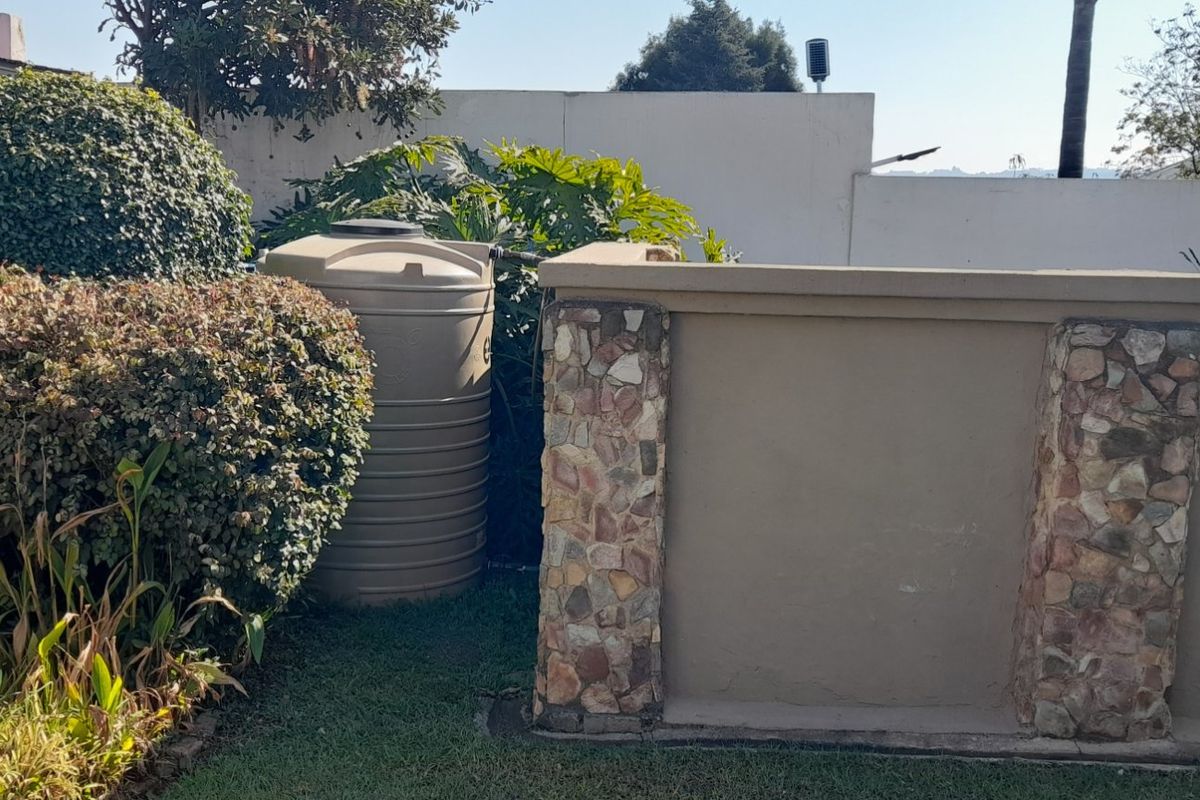 A rear garden area featuring a large water storage tank positioned against a stone-clad and plastered boundary wall.