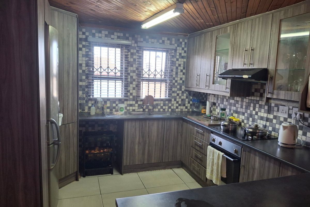 Functional kitchen featuring wood-look cabinetry, dark countertops, mosaic tile backsplash, and a timber-paneled ceiling with integrated built-in oven and hob.