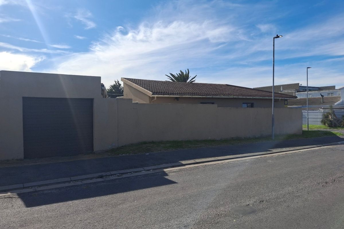 Street view of the property showing the perimeter wall, garage entrance, and tiled roof structure.