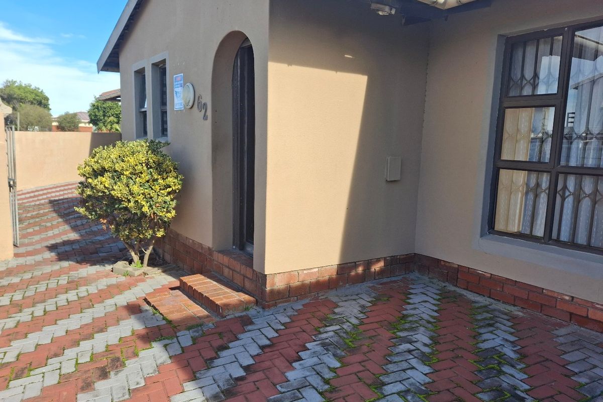 Front entrance area of the house featuring a plastered facade, arched doorway, security bars on windows, and brick-paved driveway.