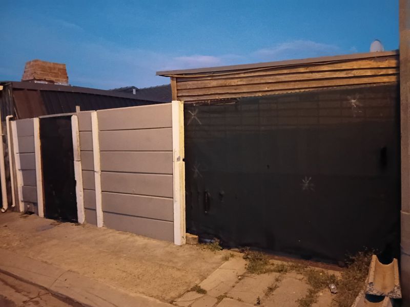 Street-facing view of the property boundary featuring a precast concrete wall and timber structure with visible signs of wear.