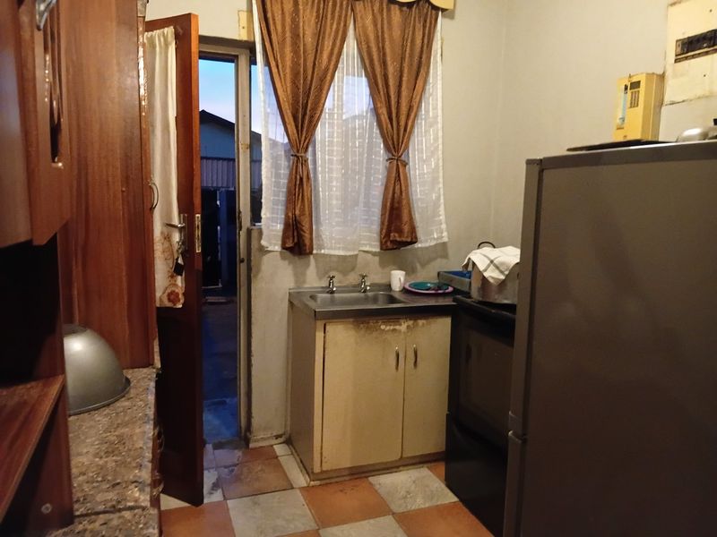 A compact kitchen area featuring basic cabinetry, a sink, and direct access to the exterior, requiring cosmetic updates and repairs to fixed finishes.