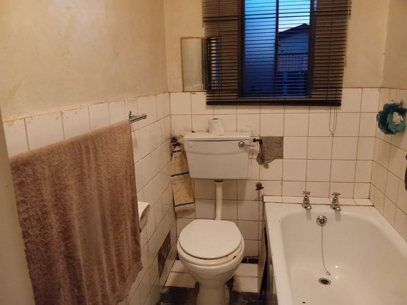 A dated bathroom featuring a standard bathtub and toilet, requiring significant renovation and repair to the wall tiling and plasterwork.