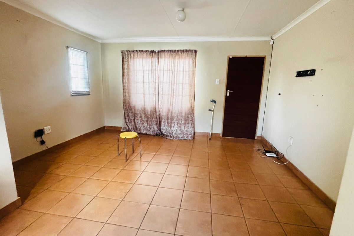A vacant living room featuring tiled flooring, neutral wall tones, and window blinds, offering a blank canvas for interior design and personalization.