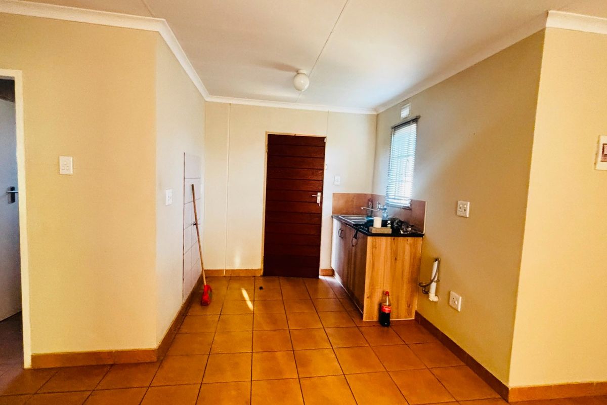 A compact kitchen area featuring tiled flooring, basic cabinetry with a sink, and a timber door leading to an adjacent space.