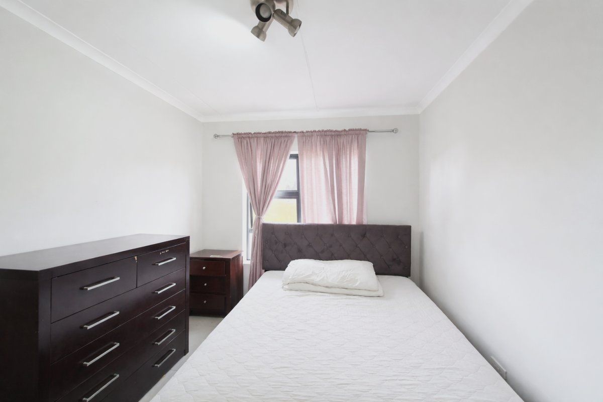 A simple bedroom featuring white walls, a ceiling-mounted spotlight, and a window with a curtain rod.