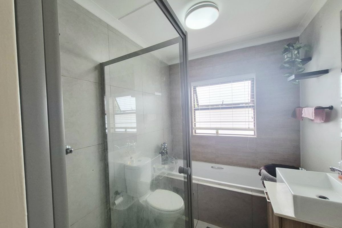 Modern bathroom featuring a glass-enclosed shower, built-in bathtub, vanity basin, and neutral tiled finishes with natural light from a window.