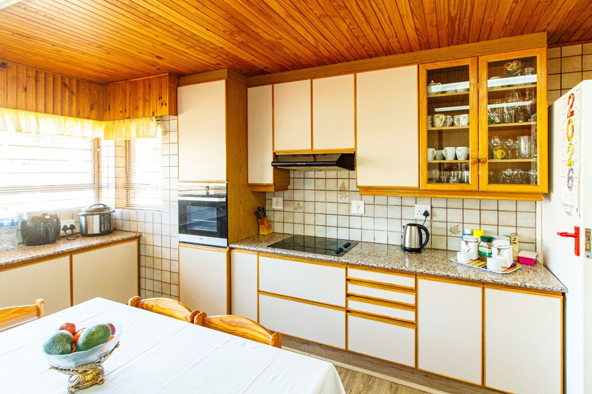A functional kitchen featuring timber ceilings, granite countertops, built-in oven, electric hob, and ample cabinetry with glass-fronted display units.