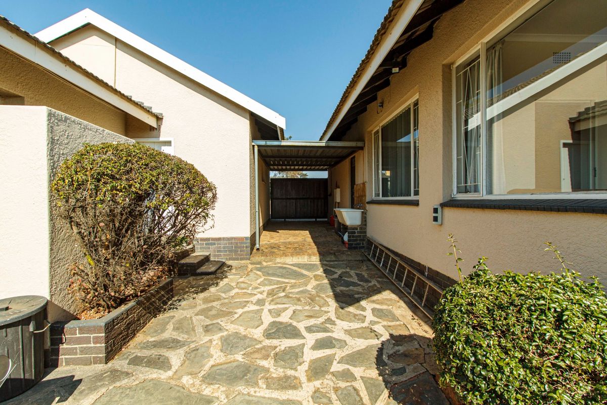 A paved rear courtyard area featuring a carport, external utility sink, and established garden beds between two building structures.