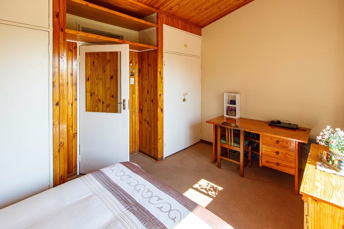 A bedroom featuring built-in cupboards, timber wall paneling, and a timber ceiling, providing a dated but functional living space.