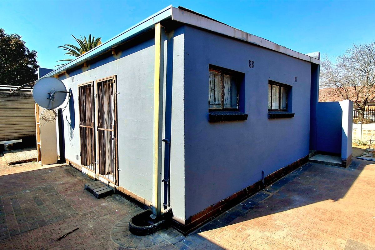 Rear exterior view of the property featuring a paved courtyard, security gates, and a satellite dish installation.