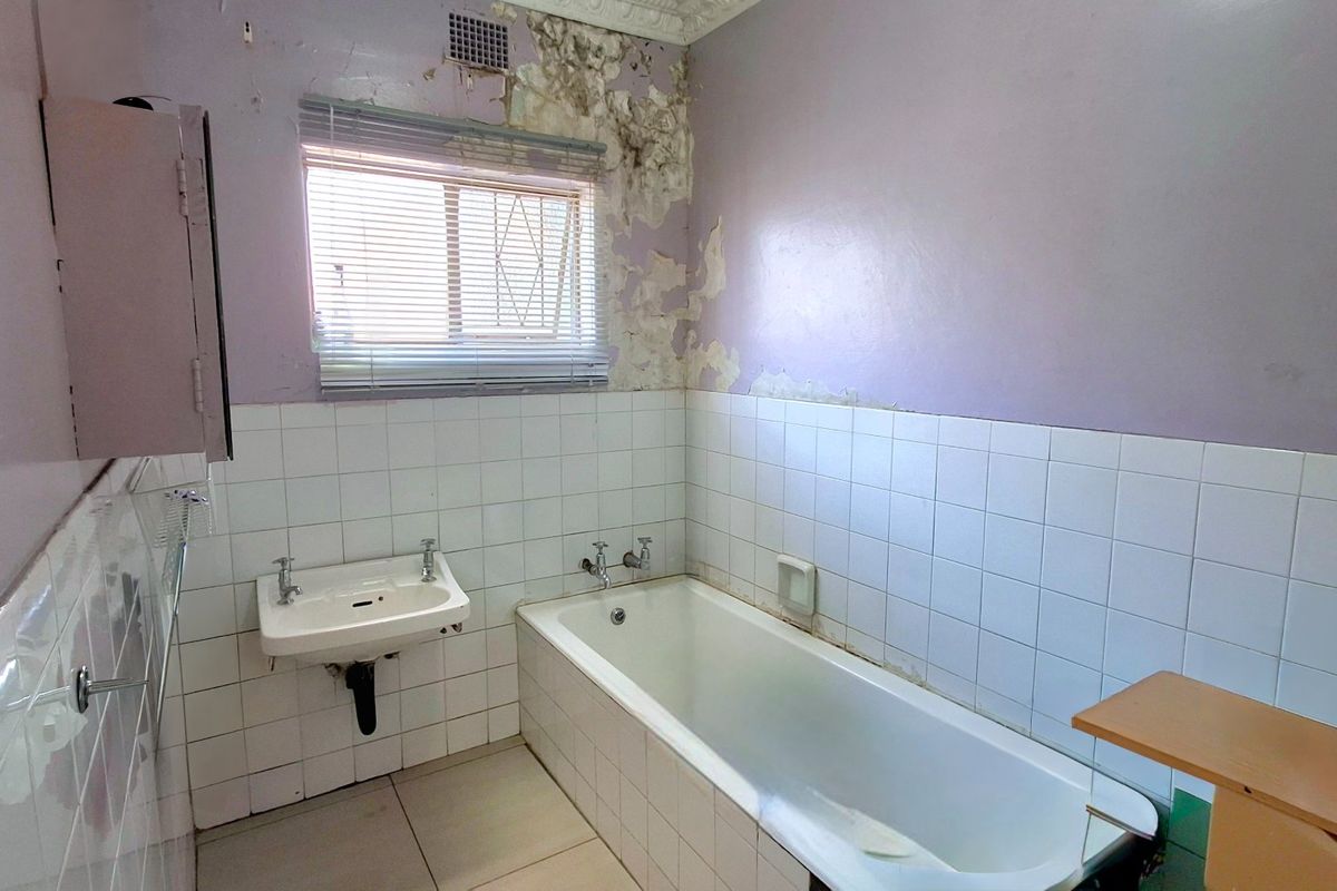 A dated bathroom featuring a built-in bathtub and wall-mounted basin, currently requiring significant wall repairs and cosmetic renovation.