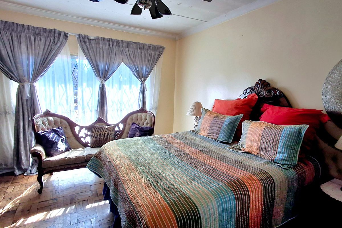 A bedroom featuring parquet flooring, a ceiling fan, and a security gate on the window. The ceiling shows visible signs of water damage.