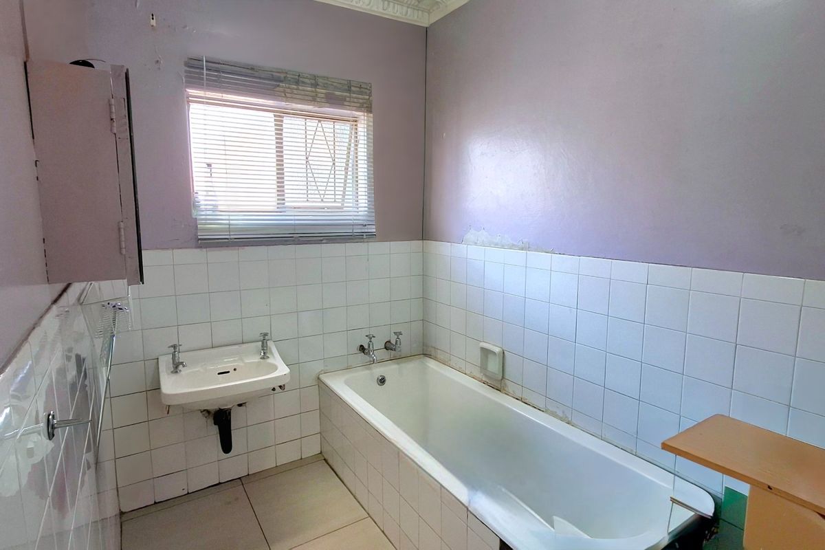 A dated bathroom featuring a built-in bathtub, wall-mounted basin, and tiled splashback, requiring cosmetic updates and wall repairs.