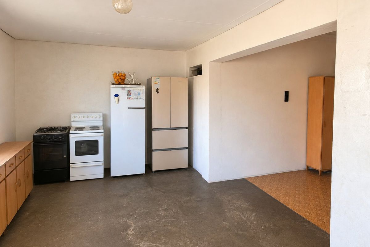 A functional kitchen area featuring built-in cabinetry, a freestanding stove, and concrete flooring, offering potential for modernization and renovation.