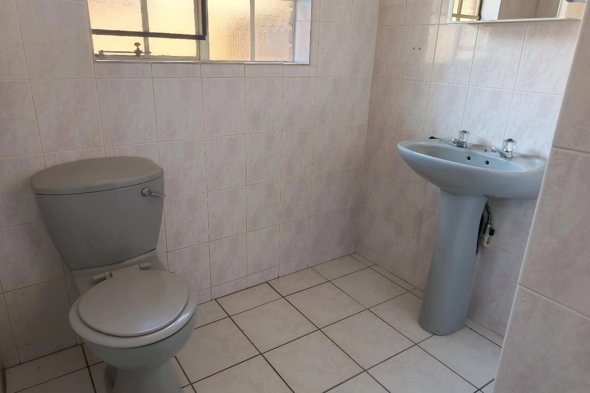 A functional, tiled bathroom featuring a pedestal basin and toilet, offering a clean and simple layout ready for potential modernization.