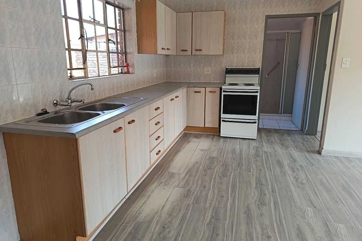 A functional kitchen featuring laminate cabinetry, a double sink, and a freestanding stove, with neutral wall tiling and modern wood-look laminate flooring.