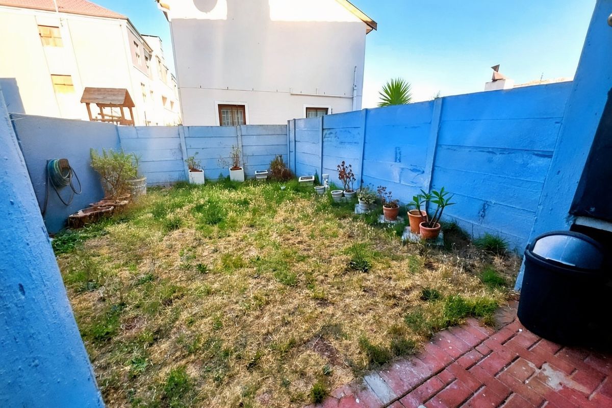 A private rear courtyard featuring a small lawn area enclosed by blue precast concrete boundary walls and a brick-paved section.