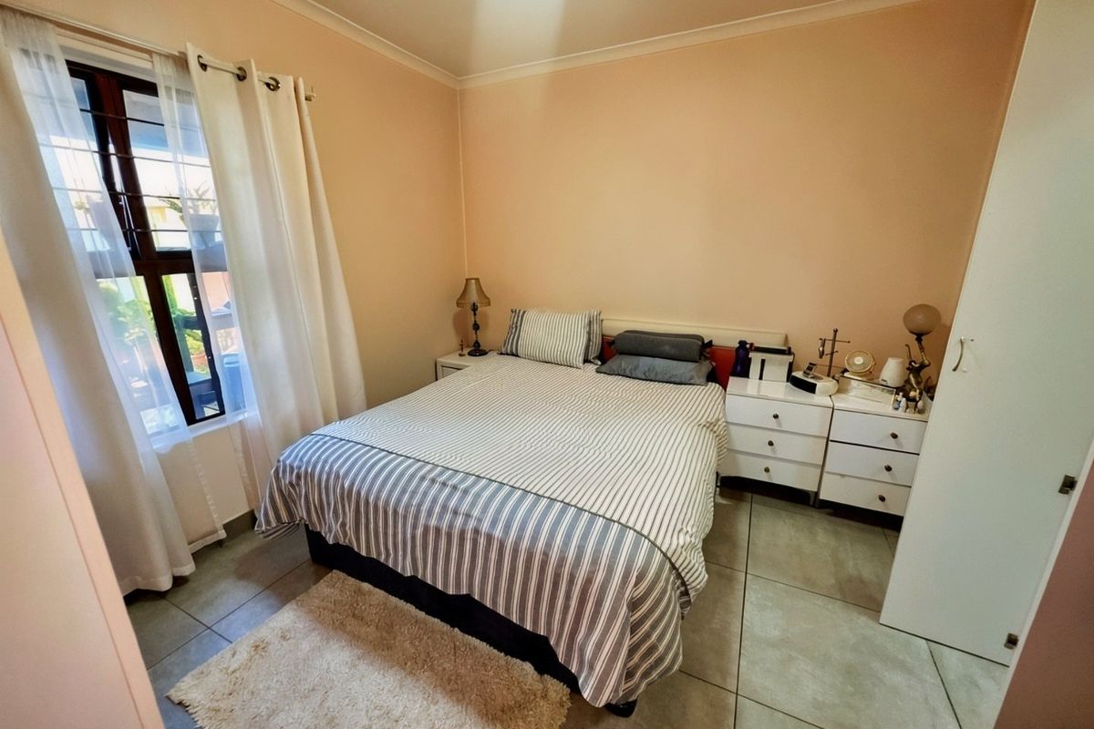 A functional bedroom featuring tiled flooring, a built-in wardrobe, and a window fitted with security bars.