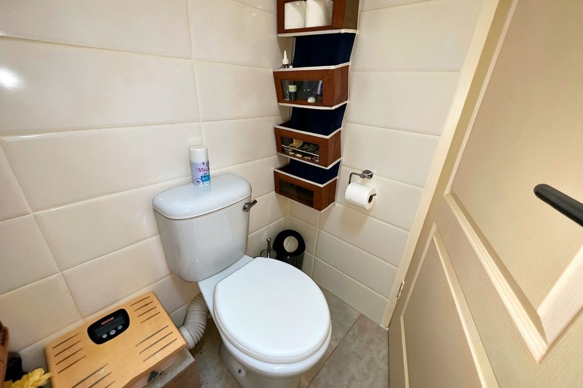 A compact bathroom featuring tiled walls and flooring, equipped with a standard toilet and wall-mounted storage.
