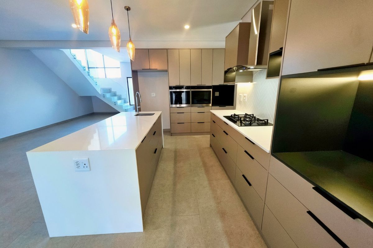 Modern kitchen featuring a central island, stone countertops, built-in oven, gas hob, and sleek cabinetry, adjacent to an open staircase.
