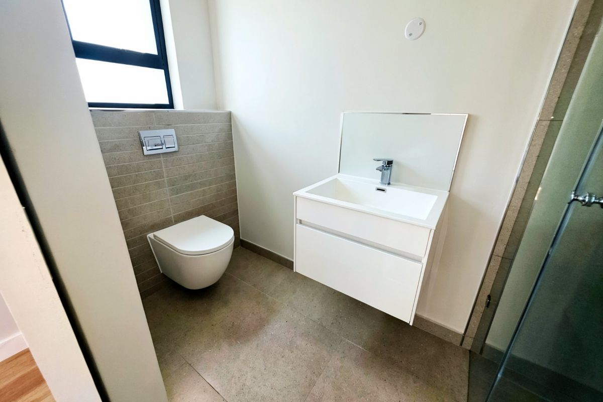 Modern bathroom featuring a wall-hung toilet with concealed cistern, sleek vanity cabinet with basin, and a glass-enclosed shower area.
