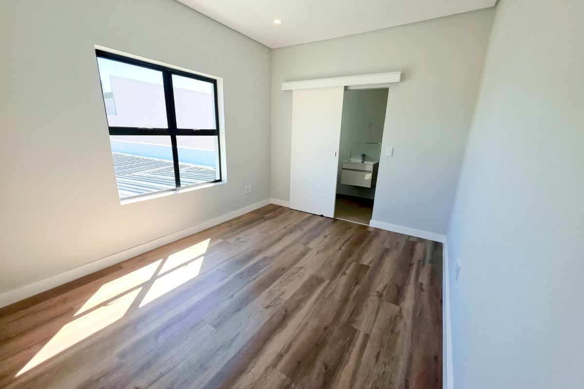 A bright, modern bedroom featuring wood-look laminate flooring, recessed lighting, and a sliding barn door leading to an en-suite bathroom.