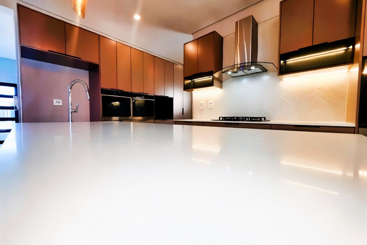 Modern kitchen featuring sleek copper-toned cabinetry, a large white quartz island, integrated appliances, and elegant herringbone backsplash with ambient under-cabinet lighting.