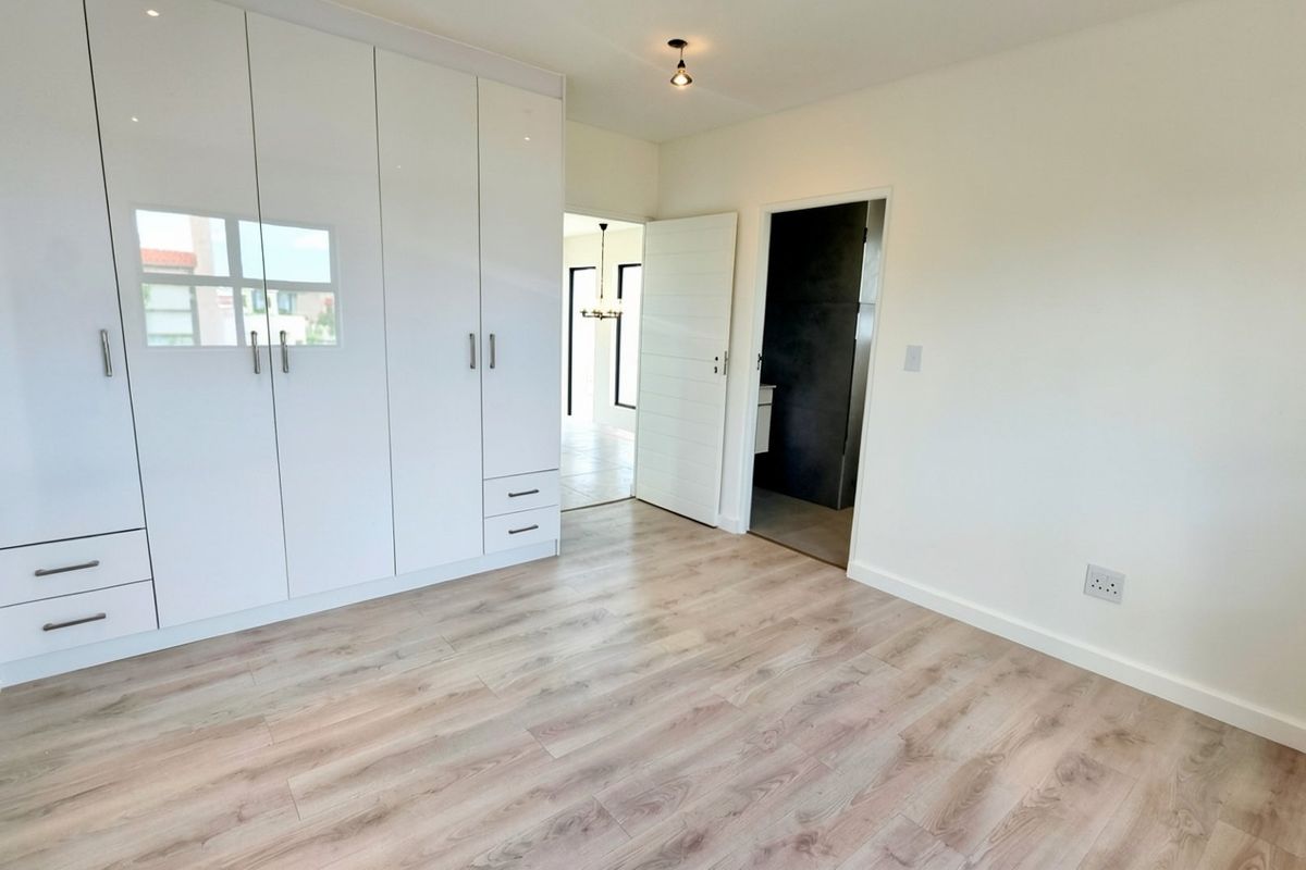A bright, modern bedroom featuring light wood-look laminate flooring and extensive white built-in cabinetry, offering a clean and neutral living space.