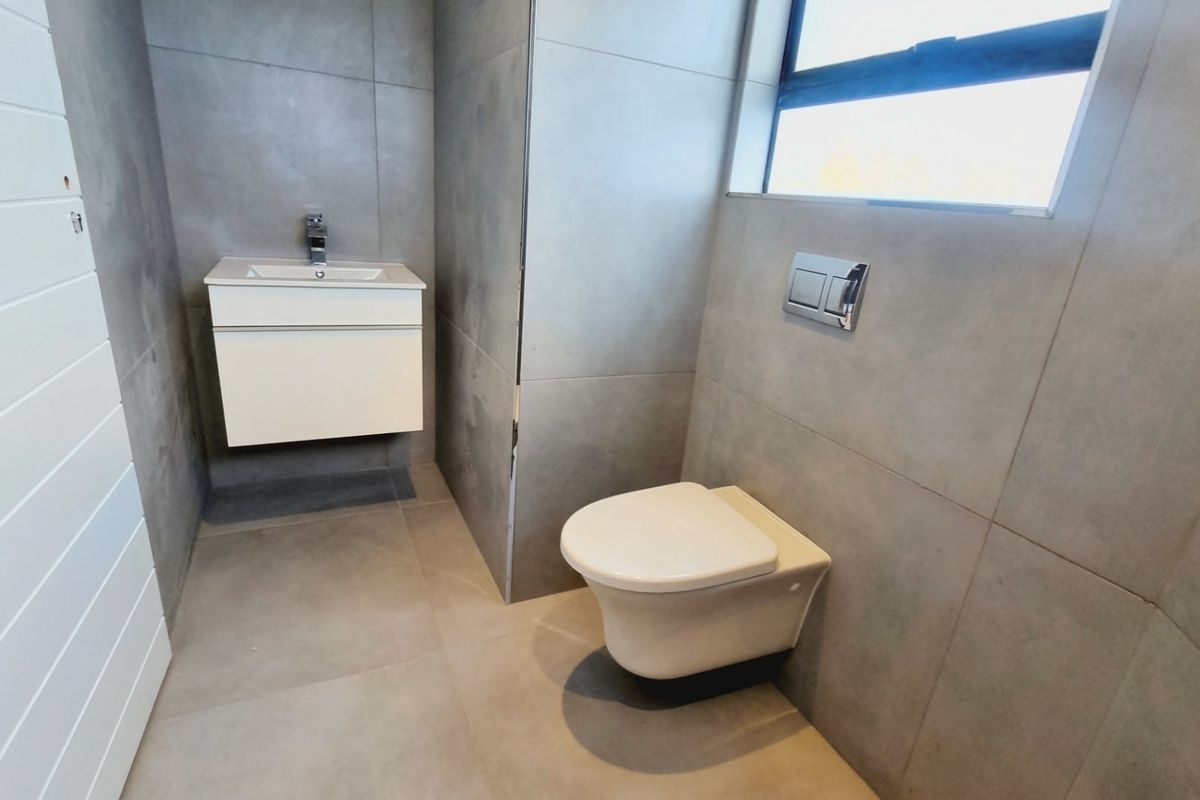 Modern bathroom featuring large format grey tiling, a wall-mounted vanity with a sleek mixer tap, and a wall-hung toilet with a concealed cistern.