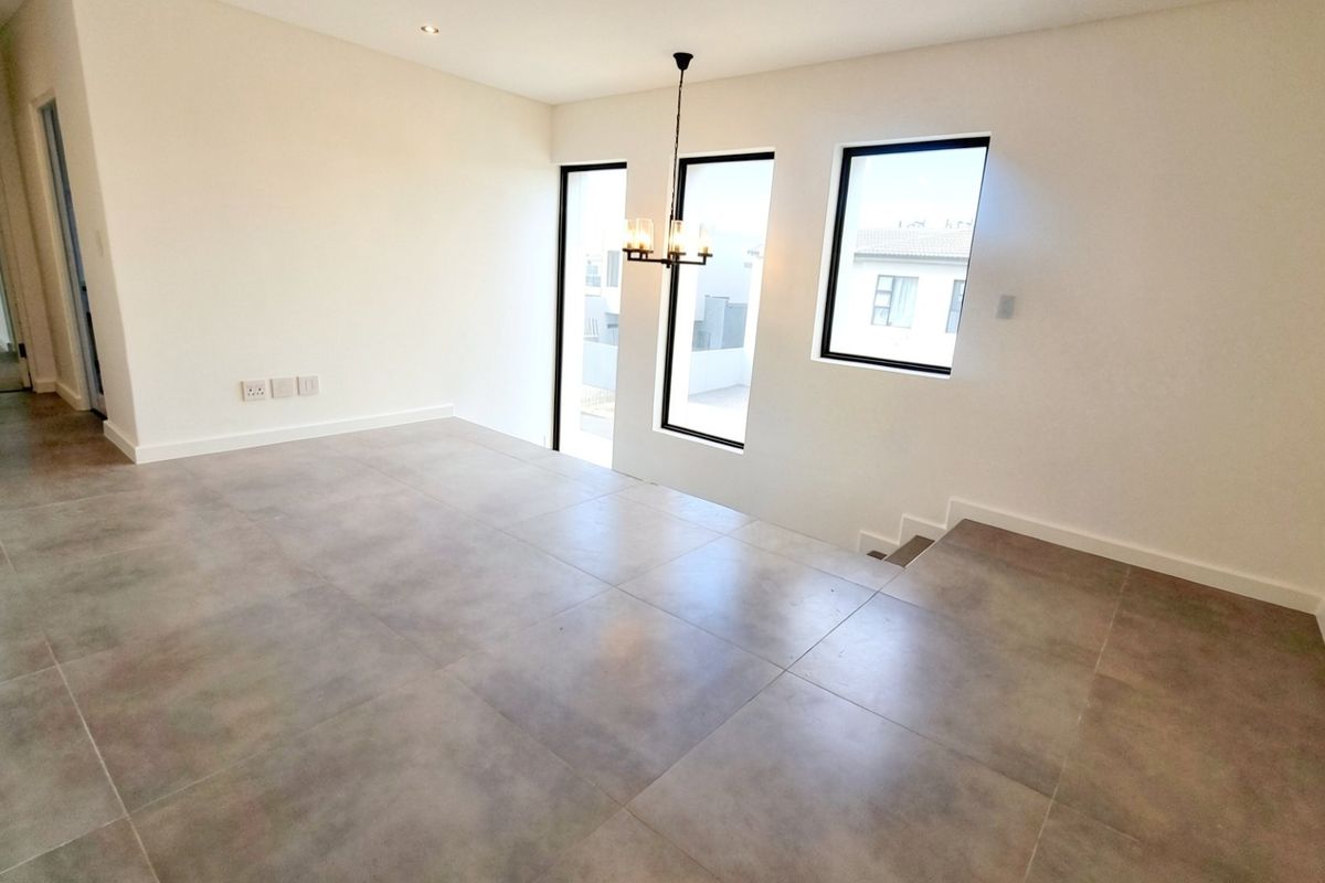 A bright, modern, and vacant living area featuring large windows, neutral tiled flooring, and contemporary lighting fixtures, ready for personalization.