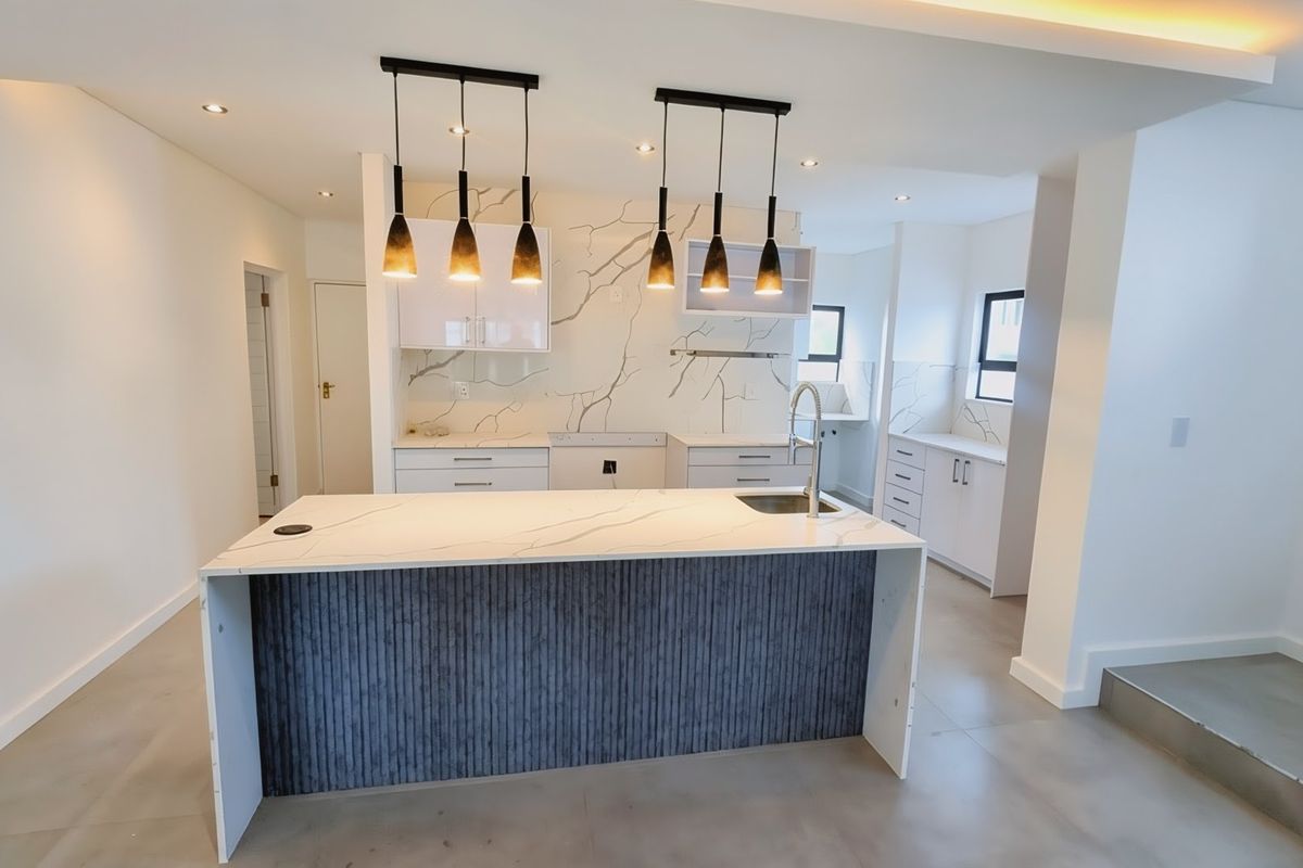 Modern kitchen featuring a central island with quartz countertops, sleek cabinetry, and contemporary pendant lighting in a bright, open-plan layout.