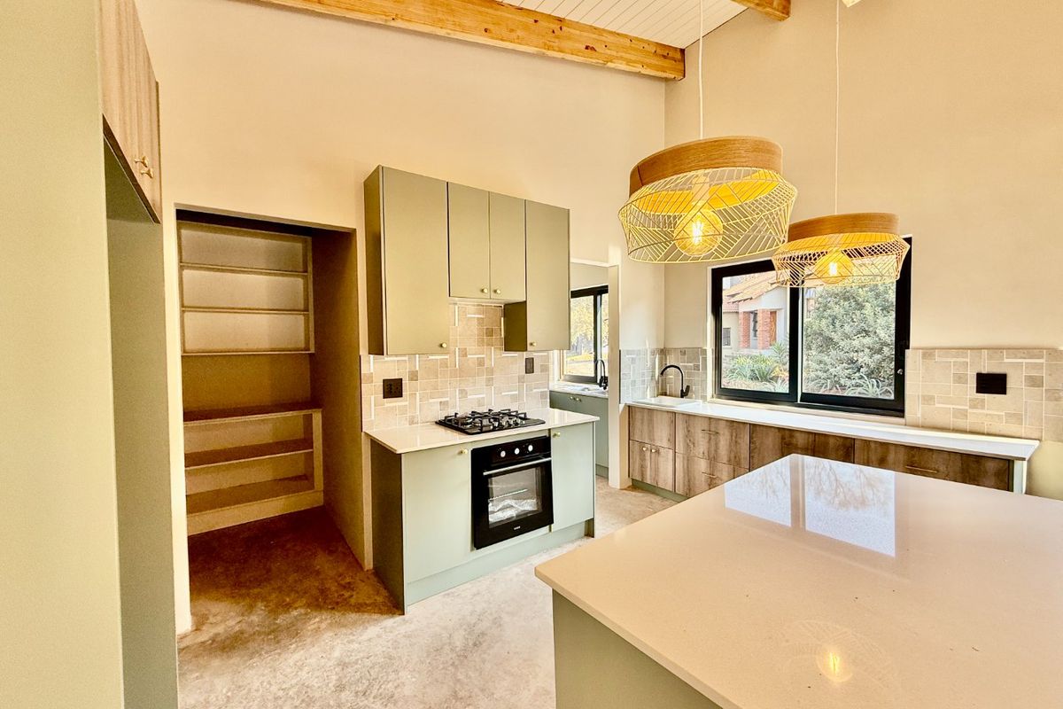 Modern kitchen featuring sage green cabinetry, stone countertops, built-in oven, gas hob, and exposed timber ceiling beams, with an adjacent walk-in pantry.