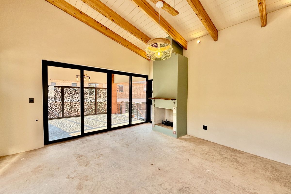 Spacious living area featuring a vaulted ceiling with exposed timber beams, a built-in fireplace, and large sliding doors opening to an outdoor patio.