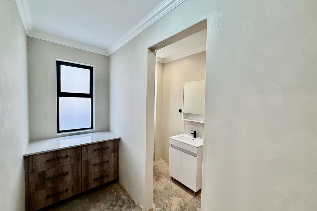 A partially renovated bathroom area featuring a modern vanity, stone-topped cabinetry, and a clean, neutral aesthetic awaiting final flooring installation.