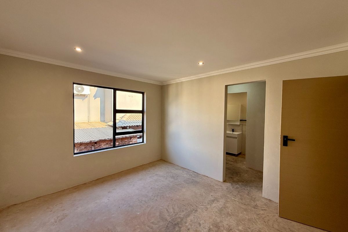 A vacant bedroom featuring neutral walls, recessed downlights, and an adjoining en-suite bathroom. The room requires final flooring installation to complete the space.