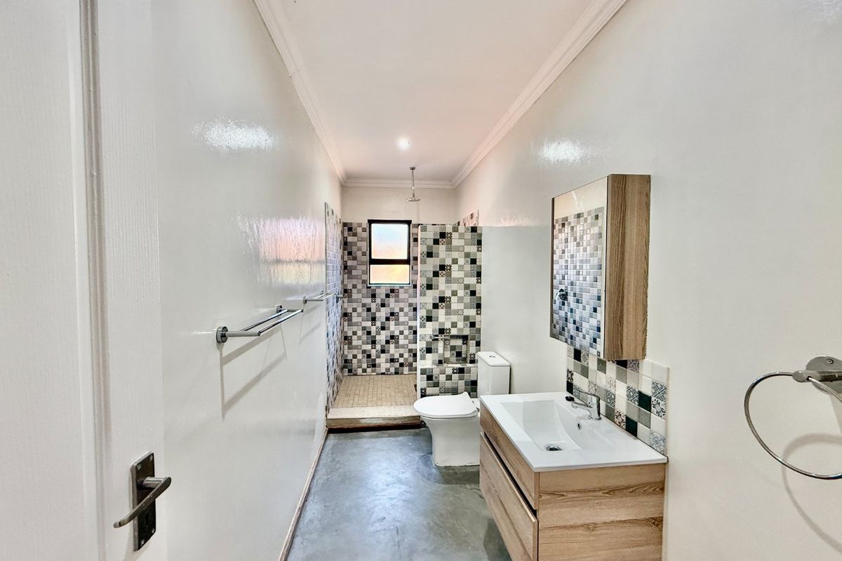 A modern bathroom featuring a vanity with basin, a walk-in shower with decorative mosaic tiling, and a toilet, finished with polished concrete flooring.