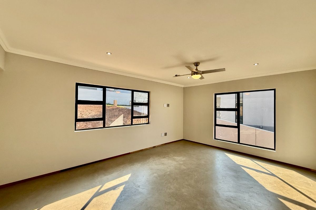 A bright, empty living area featuring polished concrete floors, modern aluminium-framed windows, a ceiling fan, and recessed lighting.