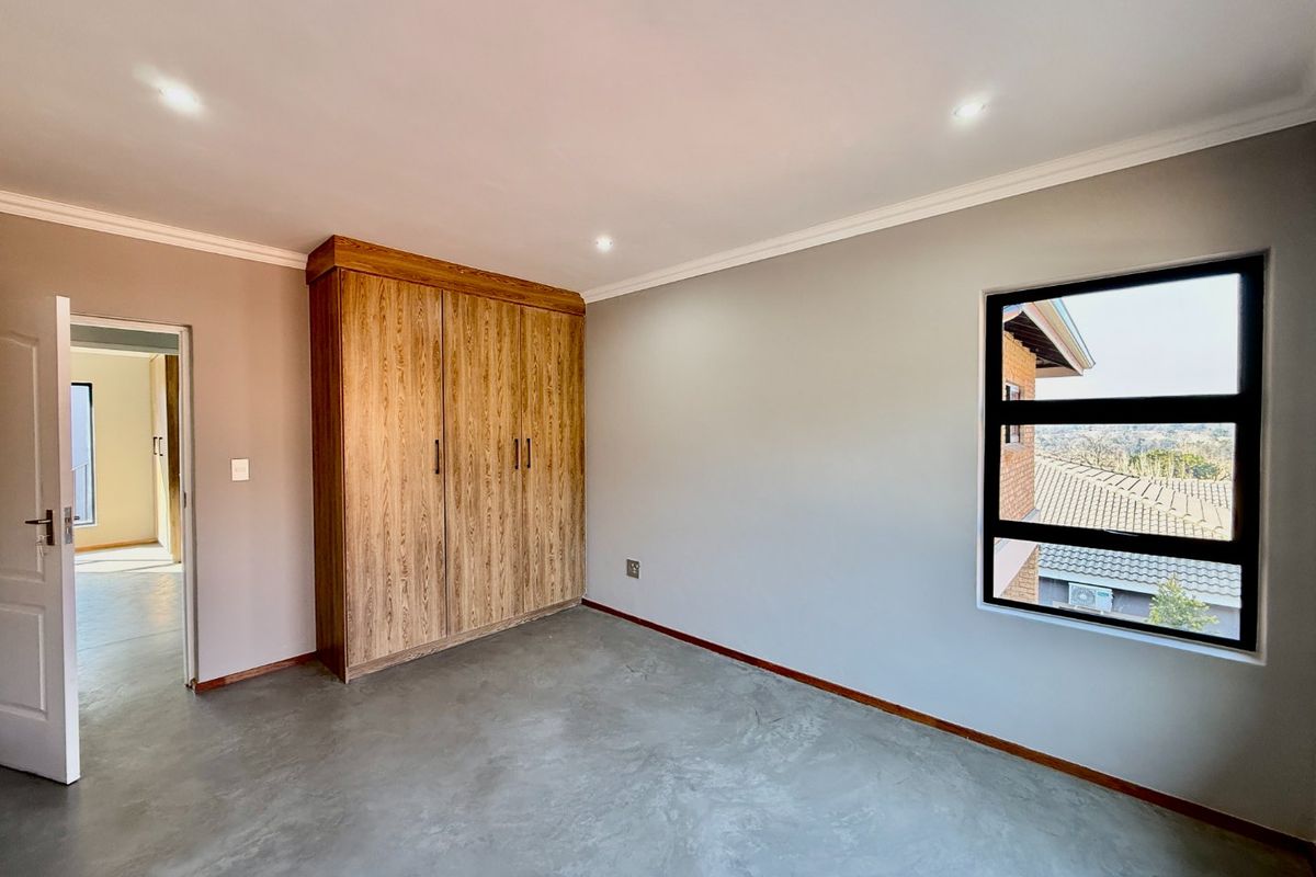 A bright, empty bedroom featuring polished concrete floors, a built-in wooden wardrobe, and recessed downlighting with a view of the surrounding area.
