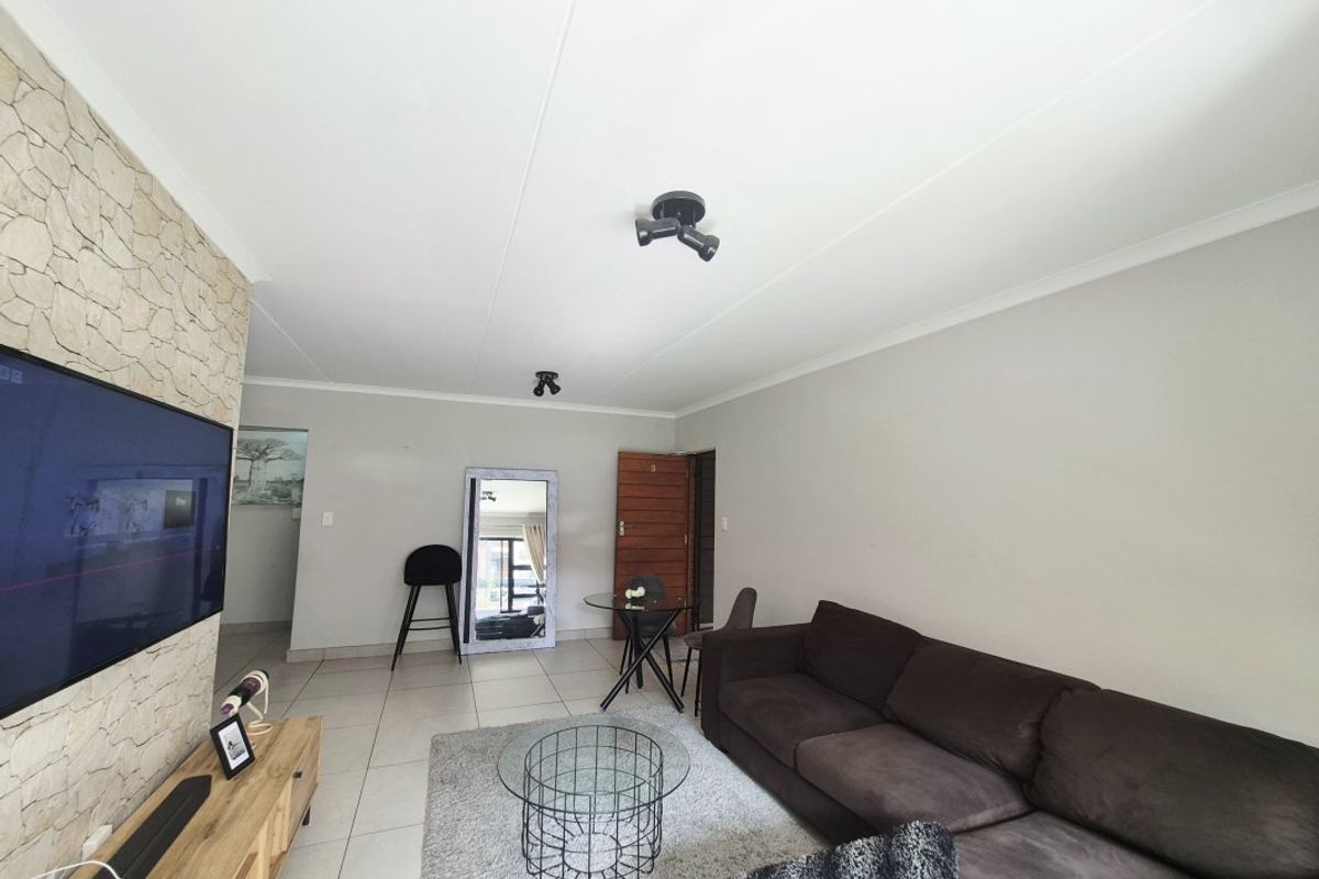 A well-maintained living room featuring a stone accent wall, neutral tiled flooring, and modern spotlight fixtures, offering a clean and functional living space.