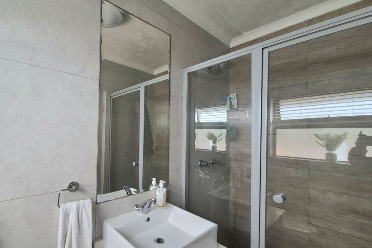 Modern bathroom featuring a vessel sink, vanity cabinet, and a glass-enclosed shower with neutral wall tiling.