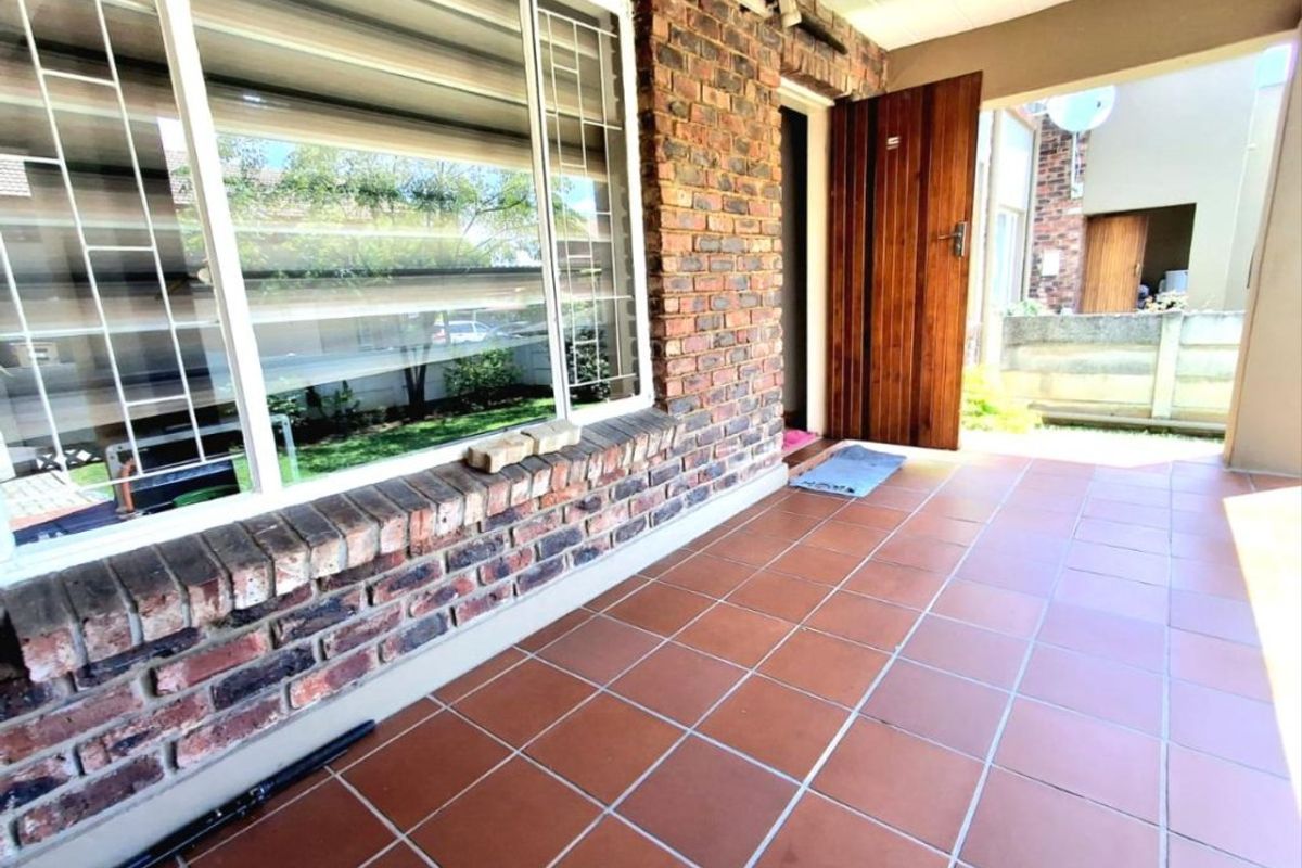 A covered patio area featuring exposed brick walls, tiled flooring, and a timber entrance door, providing a functional outdoor transition space.